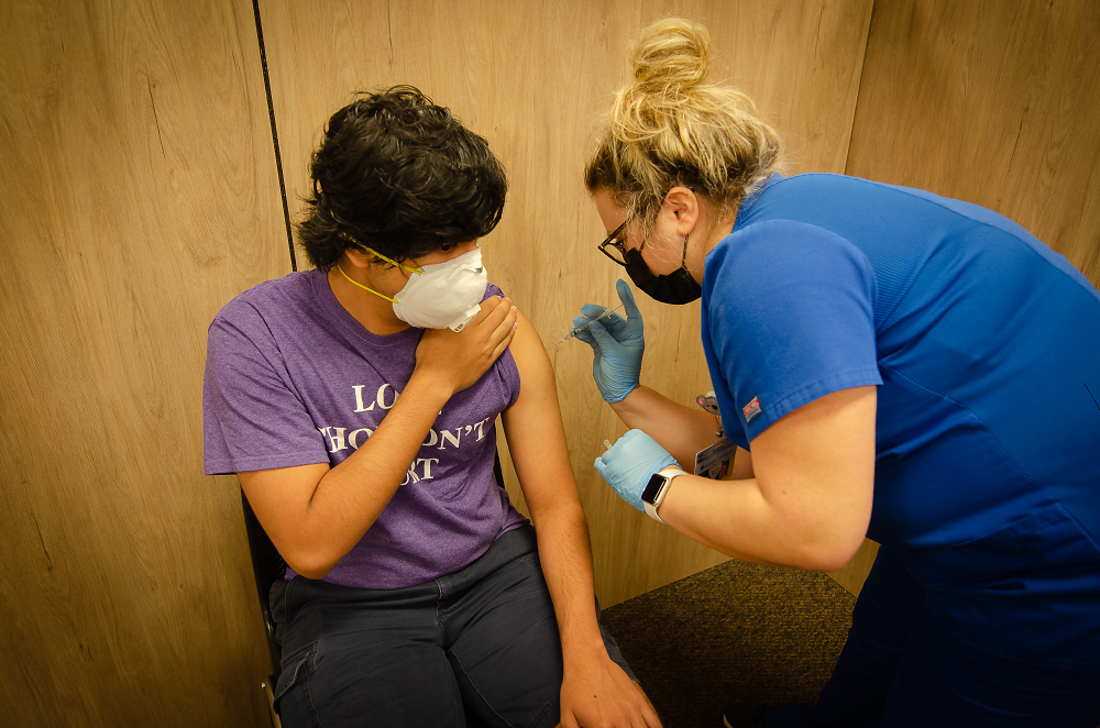 a masked woman administers a vaccine to a masked man