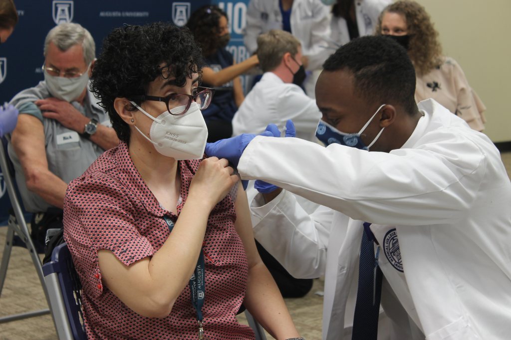 man in white coat administering a vaccine