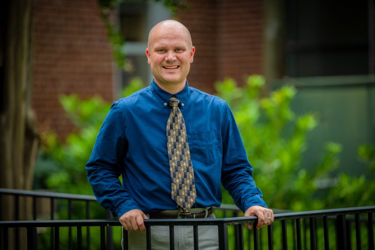Man in blue shirt and tie stands behind black railing