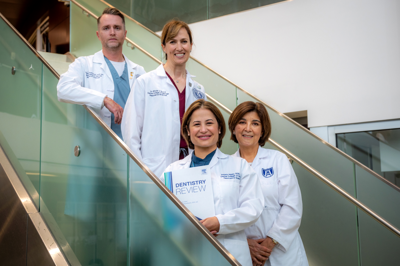 1 man and 3 women in whitecoats, standing on stairs