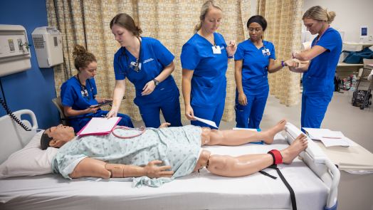 5 women nursing students standing over a mannequin