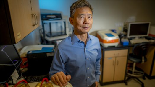 An Asian man in blue shirt stands in a lab