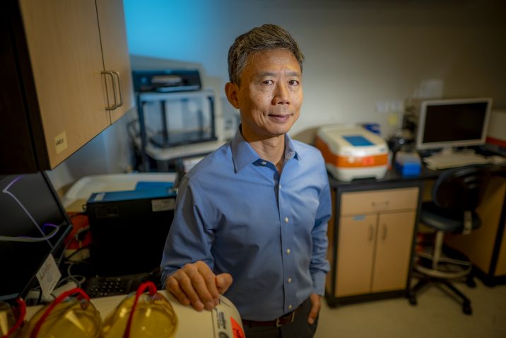 An Asian man in blue shirt stands in a lab
