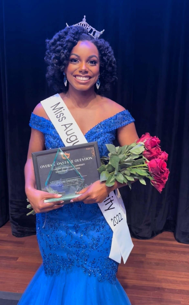 woman wearing blue dress and crown, holding roses and awards