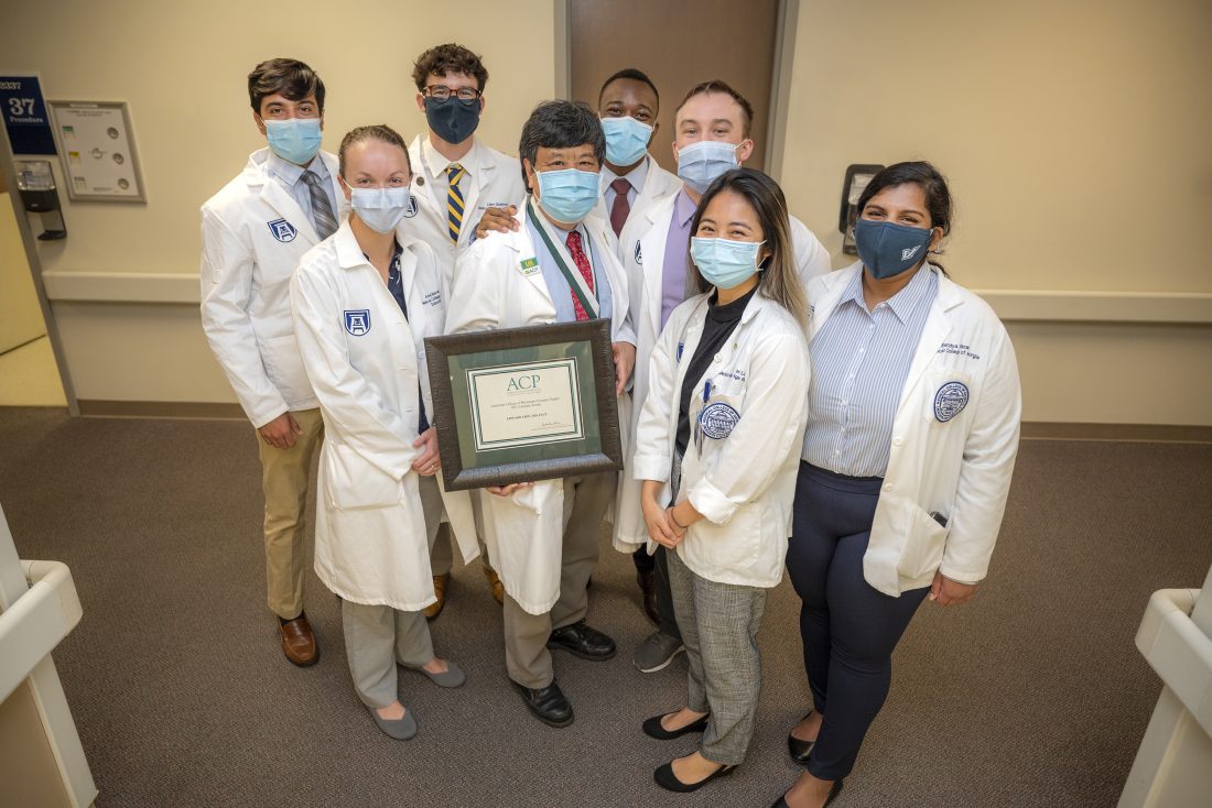 Group of masked people in white coats look at camera