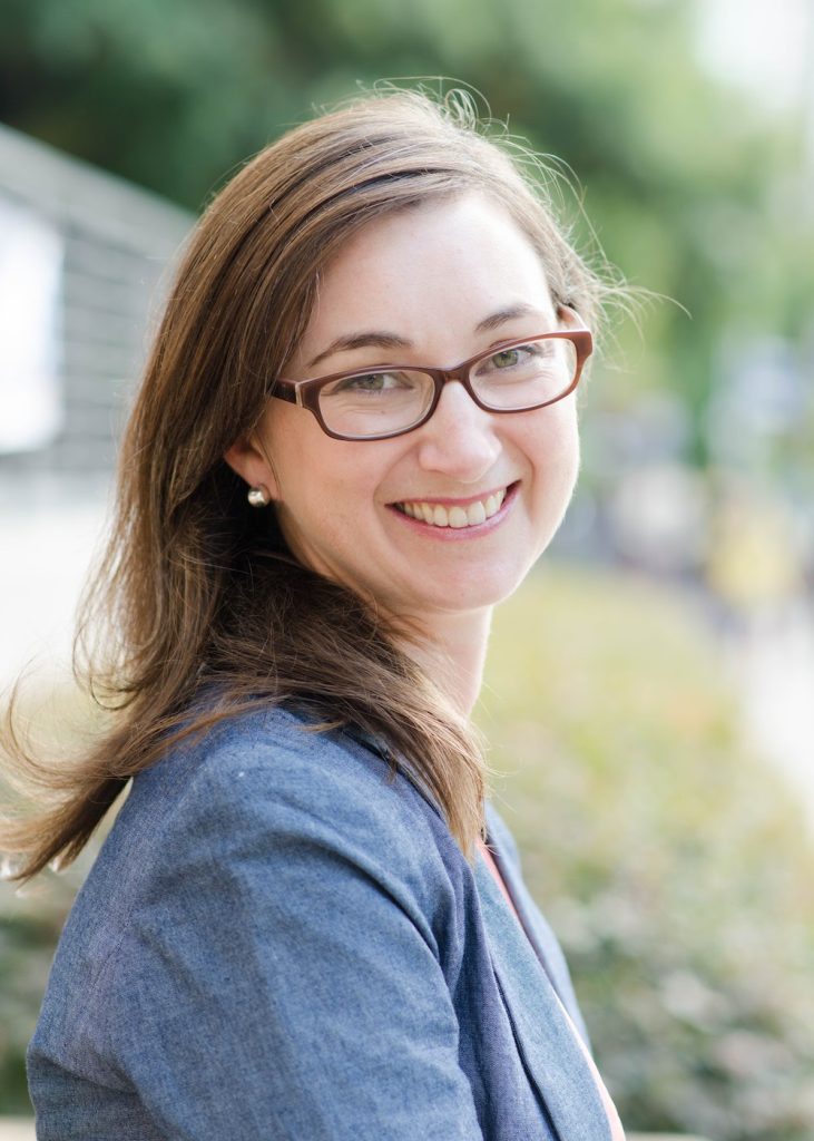 A woman in a blue blazer and glasses poses for a photo outside.