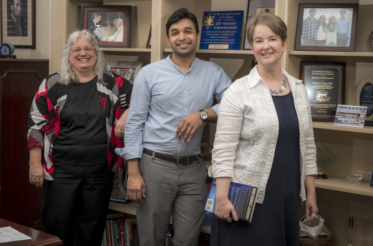 two women and man smile in front of bookshelf