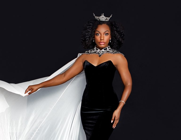 woman wearing black dress, white cape and crown