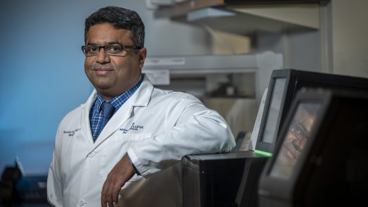 Man in white coat and glasses looks at camera