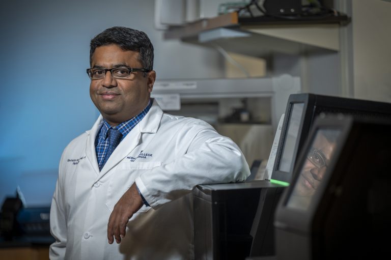 Man in white coat and glasses looks at camera