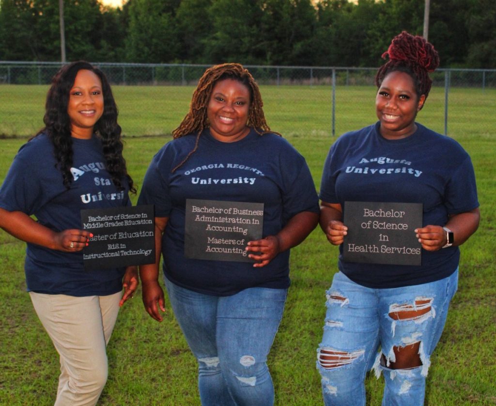 3 women holding signs indicating what degrees they have