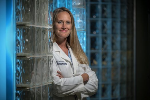 Female doctor smiling at camera leaning against a wall.