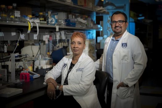 Woman sitting in lab with man standing behind her smiling at camera.