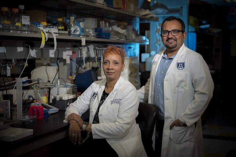 Woman sitting in lab with man standing behind her smiling at camera.