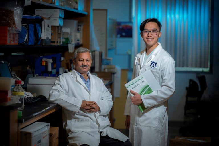 Two men in white coats smile at camera