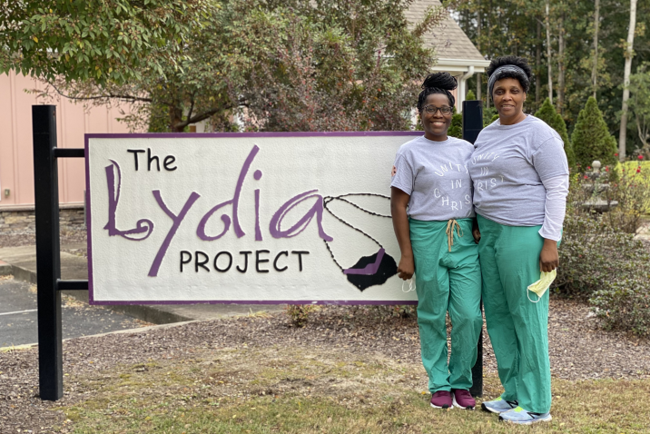 two women standing outside a sign that says "The Lydia Project"
