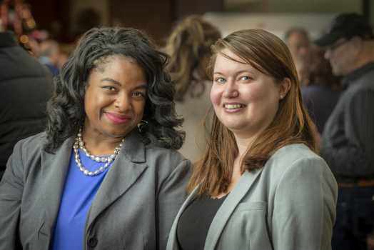 2 women in grey blazers standing together, smiling