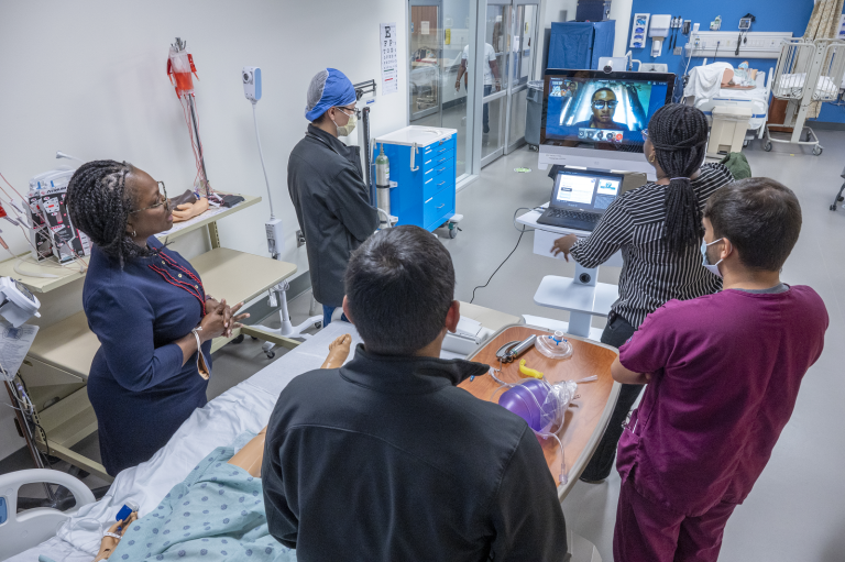 people standing around a mannequin and medical equipment, on a video call