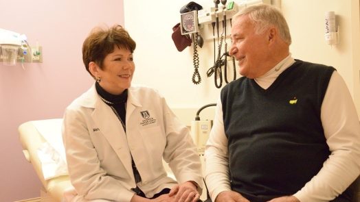 Woman in white coat sits talking with man in navy sweater