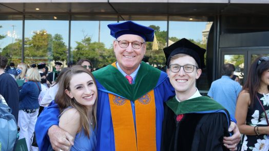 Three people embrace at MCG hooding ceremony