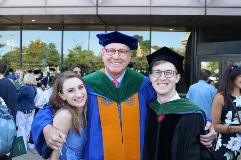 Three people embrace at MCG hooding ceremony