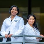 Two women in white coats stand back to back
