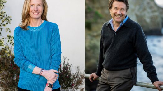 Woman in blue sweater stands, man in sweater sits on fence