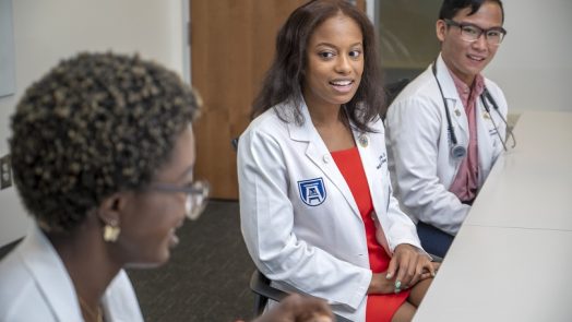 three medical students in white coats sitting at table