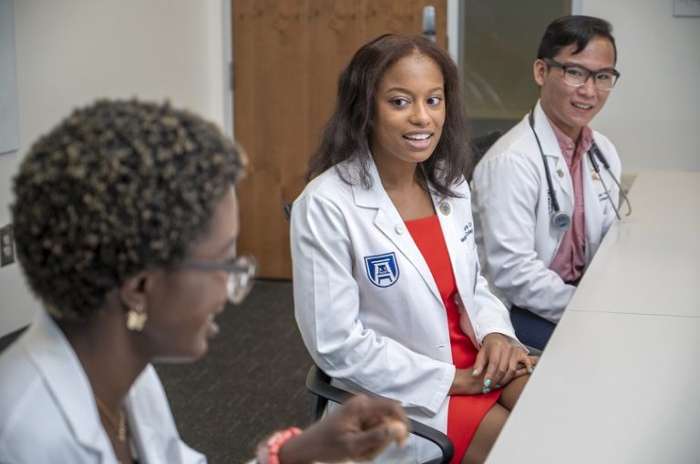 three medical students in white coats sitting at table