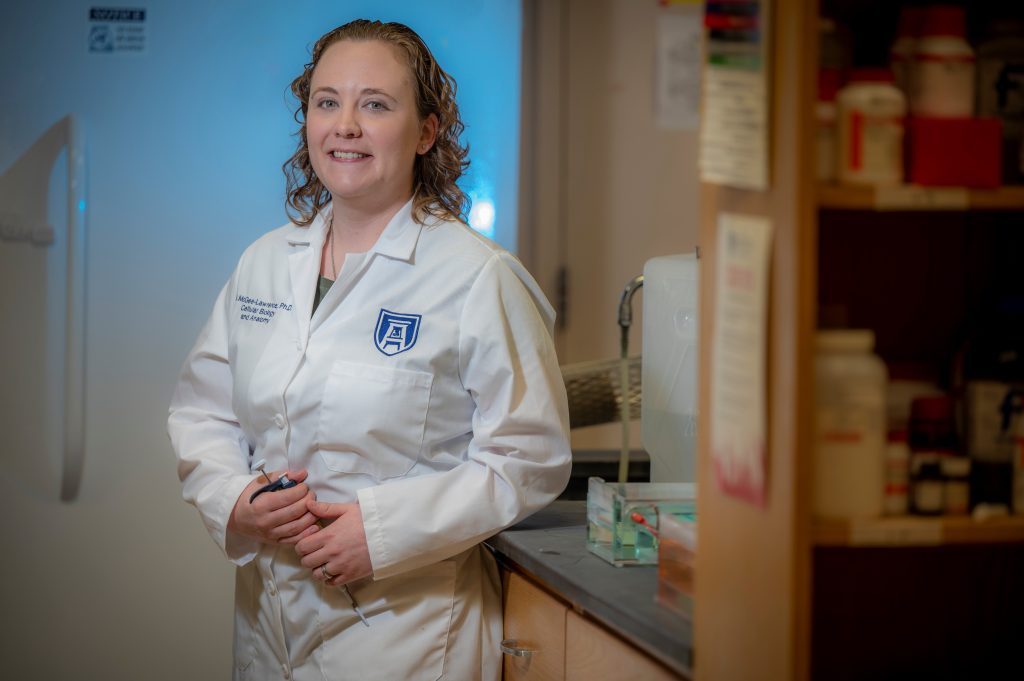 Woman with curly hair, wearing white coat stands in lab