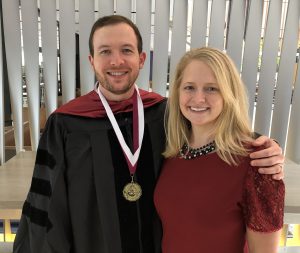 man wearing graduation regalia, beside a blonde woman