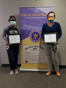 two students, wearing masks, standing in front of a poster