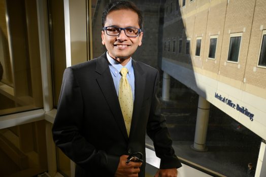 Man in dark suit and glasses standing in front of window