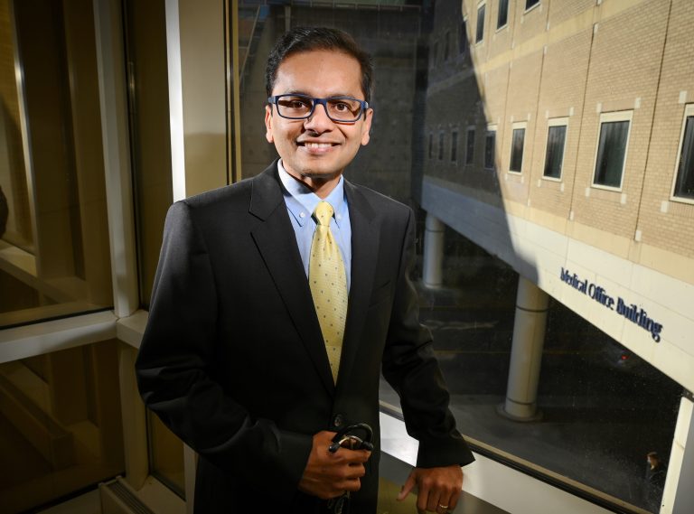 Man in dark suit and glasses standing in front of window