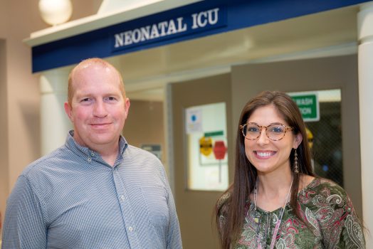 Man with red hair and woman in glasses stand in front of NICU