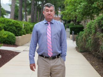 Man in blue shirt and pink tie stands on sidewalk