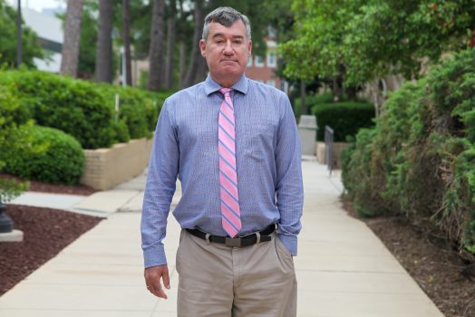 Man in blue shirt and pink tie stands on sidewalk