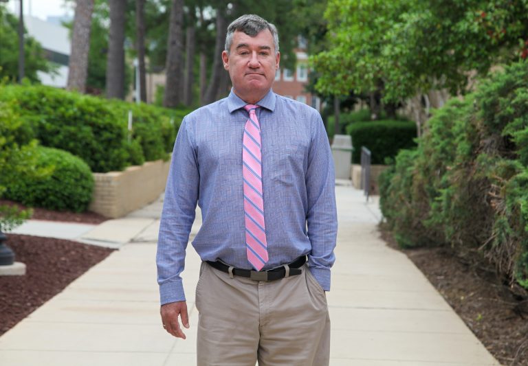 Man in blue shirt and pink tie stands on sidewalk