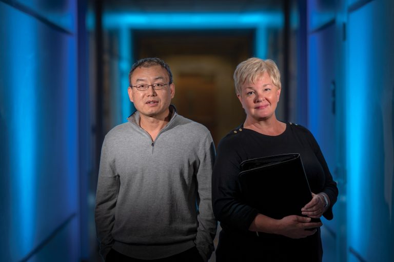 Man with glasses and woman holding book stand in hallway