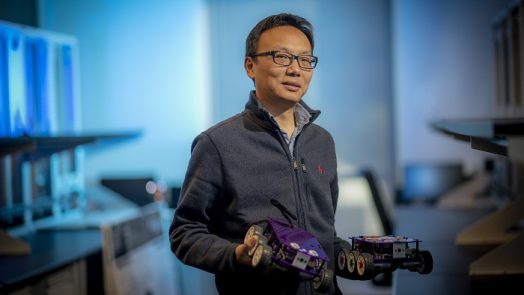 man with glasses holding two remote control cars