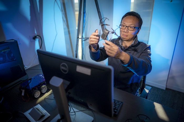 man with glasses at computer holding quadcopter