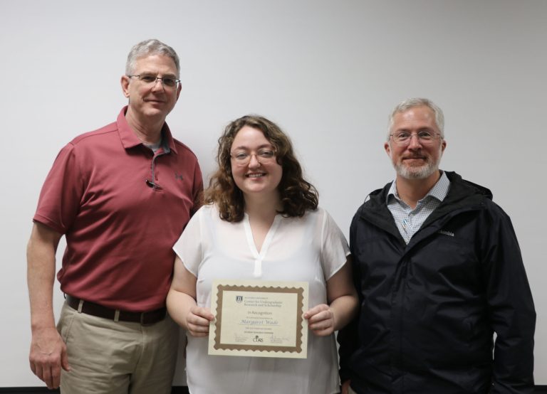 a woman stands between two men, holding a certificate