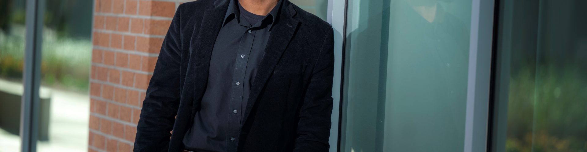 Man in black coat and shirt leans against building