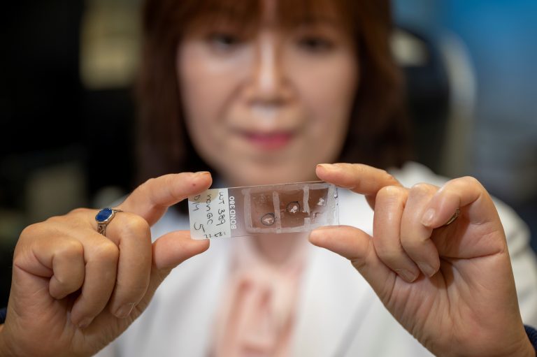 Woman holds microscope slide in foreground
