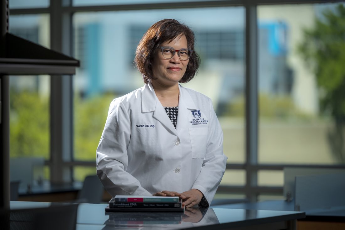 Woman in white coat and glasses stands in front of window