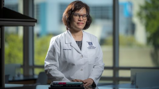 Woman in white coat and glasses stands in front of window