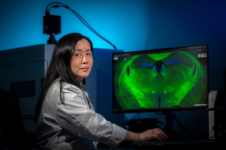 Woman with dark hair in white coat sits in front of computer