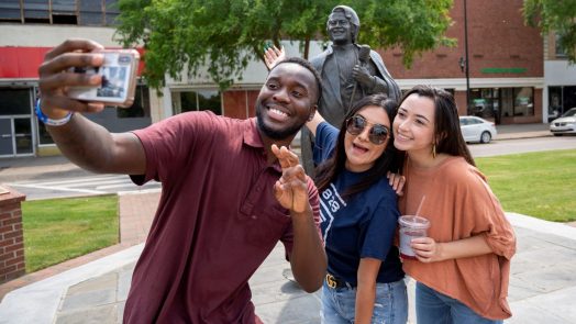 3 students taking a selfie in front of a statue downtown