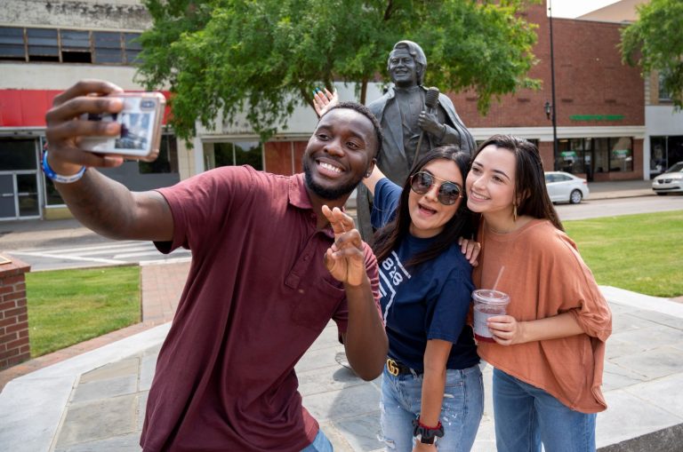 3 students taking a selfie in front of a statue downtown