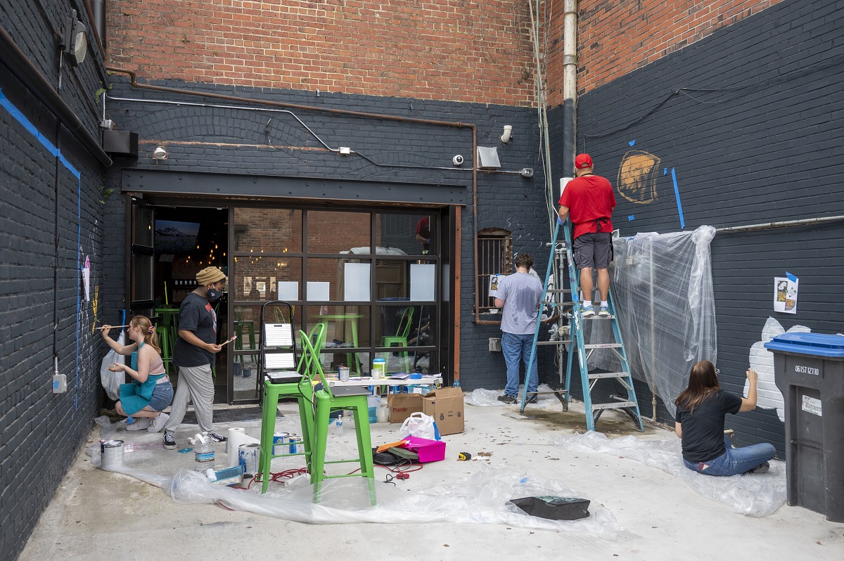 men and women paint walls of an alley